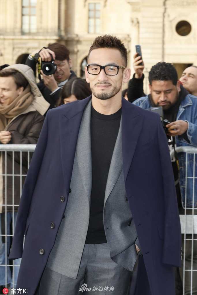 中田英寿站在秀场外，背景是灯火通明的卢浮宫金字塔，他单手插兜，微扬的下巴带着一丝不羁，长风衣的衣摆被夜风轻轻吹起。