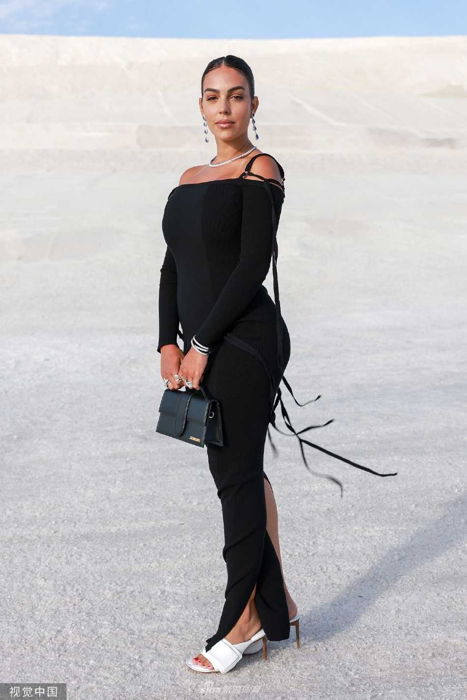 乔治娜微微低头含笑，黑色裙装的流苏细节与闪耀的钻石首饰在阳光下相映成趣，散发着温柔而坚定的魅力。