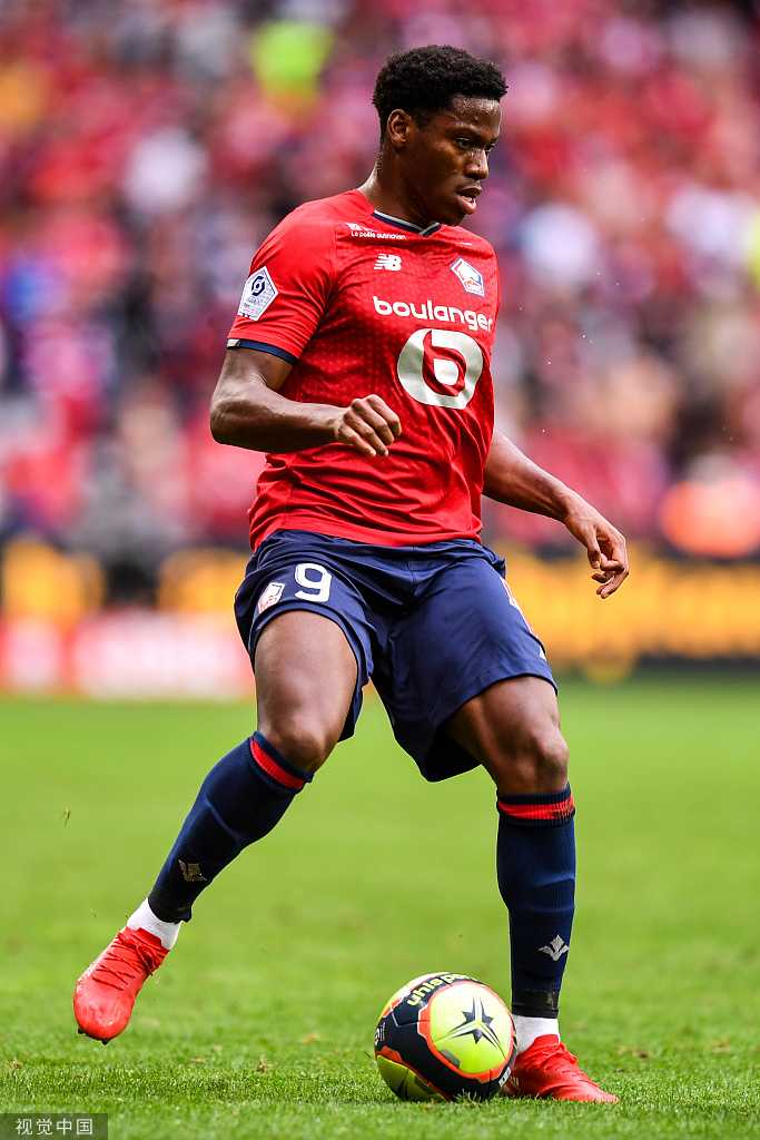 里尔球员亚兹奇在比赛中全神贯注地控球，他身边是两名蒙彼利埃防守球员的夹击，背景是巨大的球场顶棚和明亮的灯光，凸显了法甲赛场上的紧张对抗氛围。