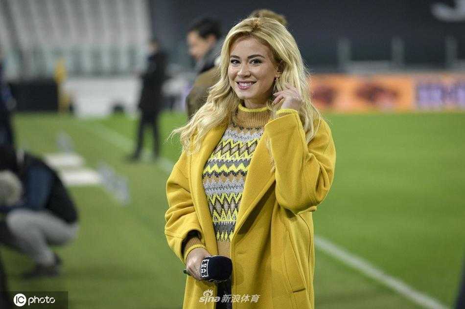 迪莱塔·莱奥塔身着一袭优雅的驼色大衣现身安联球场，金色长发披肩，她手持工作证件，微笑着面对镜头，知性气质与球场的热烈氛围完美融合。