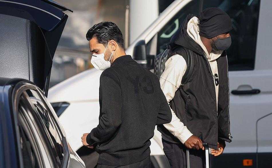 夕阳余晖中，酒店外墙上悬挂着德国足协的徽章，球员们的身影映在玻璃门上，预示着一段充满挑战与未知的征程即将开启。