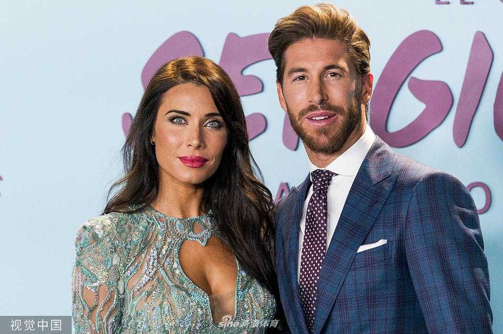 拉莫斯一袭修身西装，与身着闪耀长裙的爱妻皮拉尔在背景板前亲密合影，铁血硬汉的温柔笑意与妻子的优雅从容相得益彰，仿佛画中人。