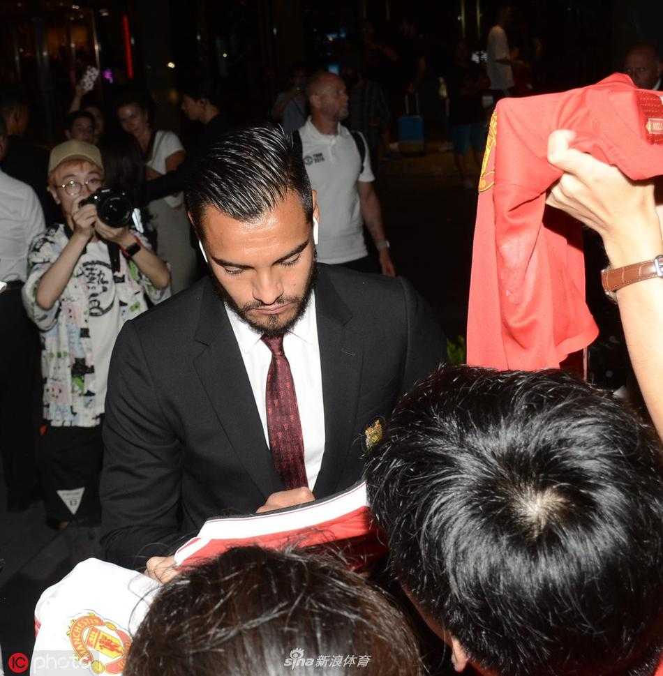 曼联球员拉什福德戴着耳机走出通道，看到热情的球迷后露出惊讶而温暖的笑容，伸手与护栏外的球迷击掌