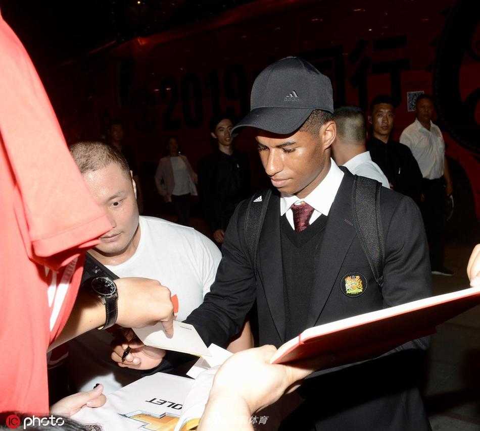 一位小球迷骑在父亲肩头，手持自己画的曼联队徽，眼中闪烁着兴奋的光芒，在人群中格外显眼