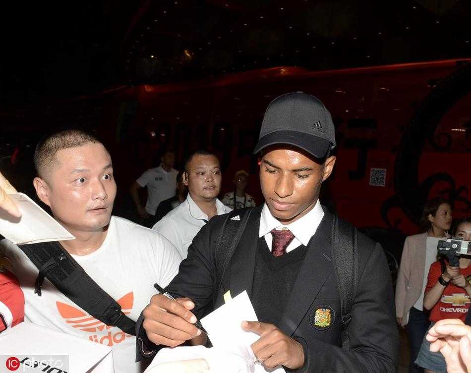 曼联主教练索尔斯克亚推着行李车走出，面带标志性的“娃娃脸”微笑，从容地向两侧的球迷点头致意