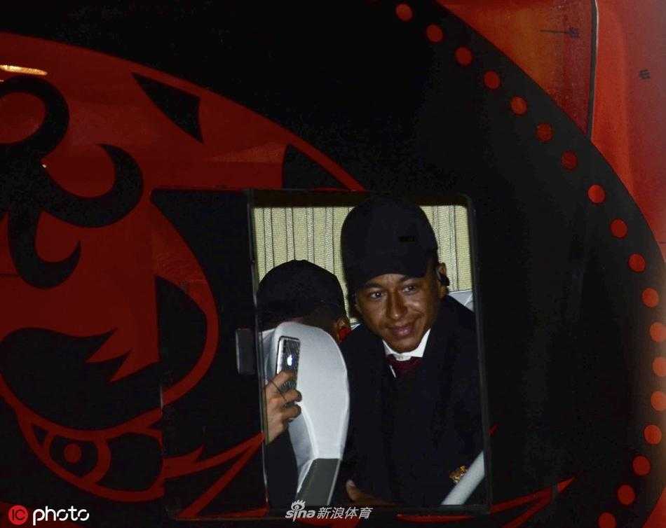 曼联球队大巴缓缓驶离机场，车身上的巨大队徽在灯光下闪耀，窗外仍有不舍的球迷追着大巴挥手道别