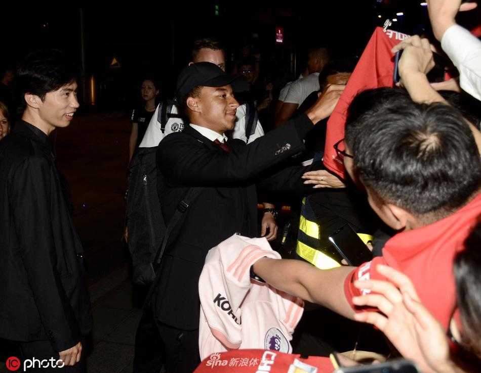 机场到达大厅内，曼联的队旗被几名球迷高高擎起，周围人群用手机记录下球队大巴启动的珍贵瞬间