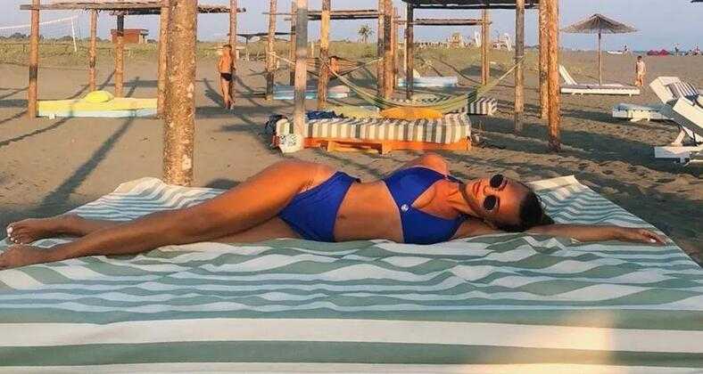 娜塔莉亚身穿碎花连衣裙，在绿荫下享受咖啡时光，桌上放着一本医学书籍，不经意间透露出她工作之外的闲暇时刻