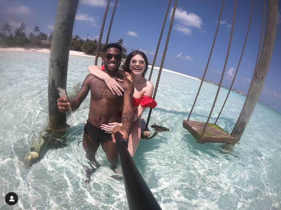 弗雷德与妻子莫妮克在夕阳余晖下的无边泳池边相拥而笑，两人手持香槟杯，身后是一望无际的印度洋，画面甜蜜得如同偶像剧海报