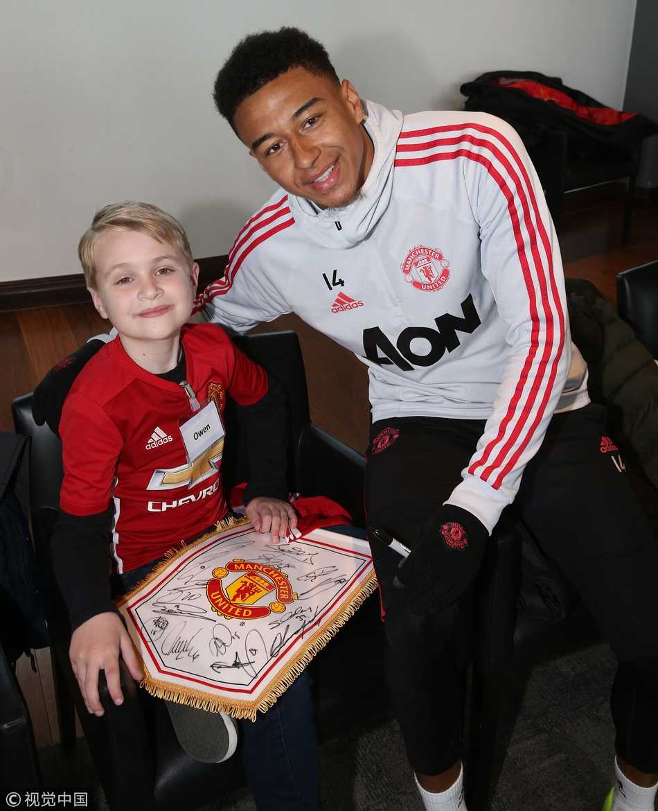 训练场的草坪上，博格巴正小心翼翼地帮助一位患有肢体障碍的小男孩颠球。博格巴用双手扶着男孩的腰，帮他保持平衡，男孩的脚成功碰到了皮球，周围的人群爆发出热烈的掌声和欢呼声。