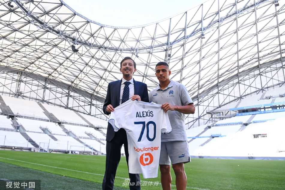 桑切斯手持马赛队围巾，面带微笑向现场媒体与球迷展示，眼中充满对新挑战的期待。