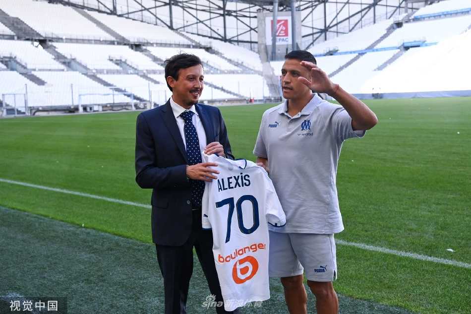 桑切斯在发布会后与马赛队徽合影，他双臂交叉，目光坚定，展现出与俱乐部并肩作战的信念。