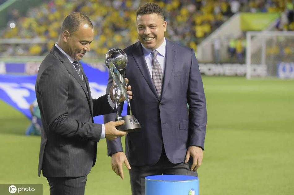 从另一个角度望去，卡福与罗纳尔多西装革履地站在展示台前，巨大的U17世界杯奖杯在聚光灯下闪耀，两人微笑着交谈，仿佛在回忆自己年少成名的岁月，也像是在为巴西足球的薪火相传感到欣慰。