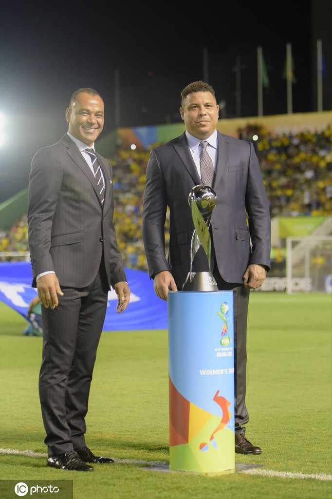 巴西传奇队长卡福面带微笑，双手稳稳捧着U17世界杯冠军奖杯，眼神中满是对后辈的赞许与对国家未来的期许，身旁的罗纳尔多神情专注，仿佛看到了当年的自己。