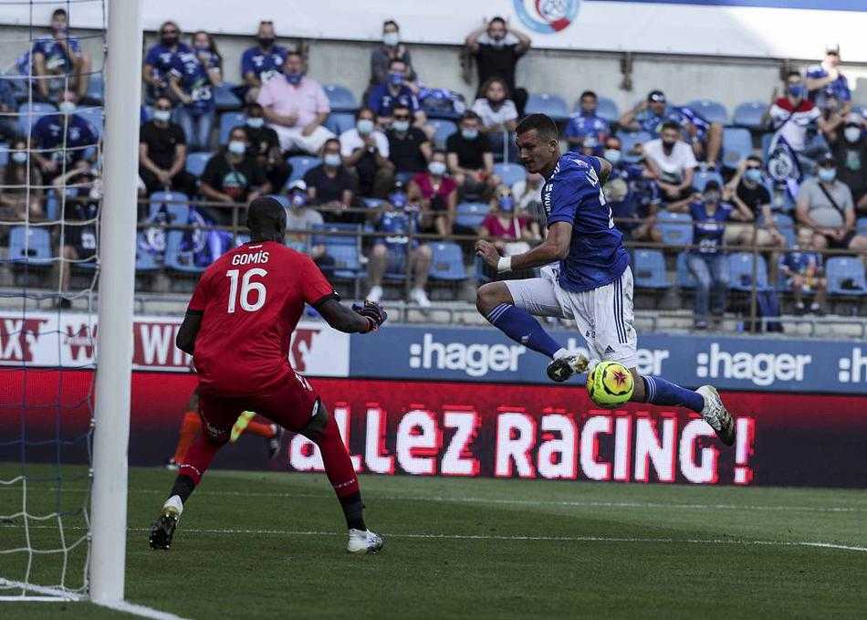 白衣主队球员带球推进，身边是两名贴身紧逼的对方后卫，三人之间的攻防博弈张力十足