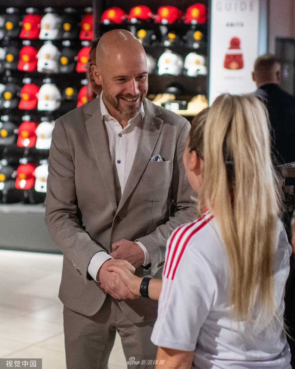 滕哈赫手持曼联围巾，向镜头外的红魔球迷们挥手致意，脸上洋溢着淡淡的微笑，这个动作是传统的新任主帅与球迷群体的首次视觉连接与问候。