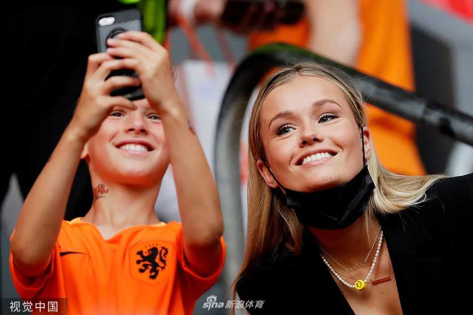 阳光洒在看台上，德容的女友米奇-基梅尼轻抚脸颊，举手投足间散发着优雅气质，成为场内一道亮丽的风景。