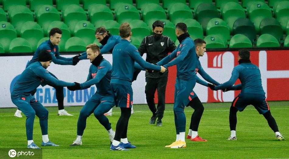 镜头拉远，捕捉到塞维利亚全队在训练场上围成一圈，进行着高强度的逼抢演练。夕阳的余晖洒在他们身上，勾勒出一幅为胜利而战的剪影。