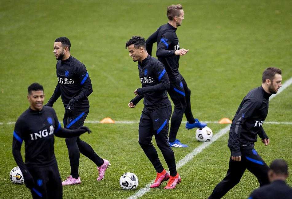 深秋黄昏的训练场上，荷兰国家队球员们神情专注，弗兰基·德容正低头认真聆听助教的战术指导，身后的队友在进行抢圈热身，空气中弥漫着大赛前的紧张与期待。