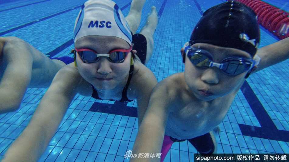 泳池边的教练正全神贯注地观察着水中训练的少年，他身体微微前倾，一只手正比划着动作要领，眼神里满是专业与期待，仿佛在雕琢一件未来的艺术品。