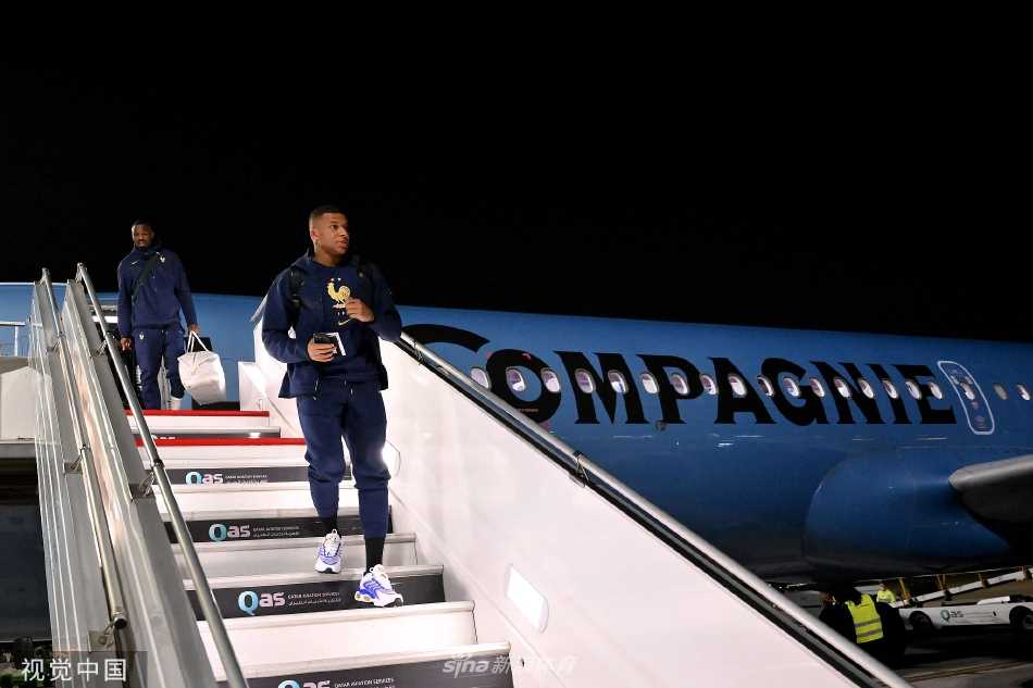 法国队队员步出机场通道，身影在玻璃幕墙的映衬下显得坚定而充满力量，开启新的征程