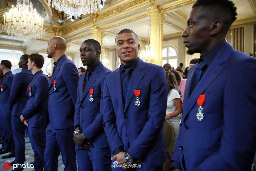 一枚刚刚授予球员的荣誉军团勋章被定格特写，精致的五辐金质徽章镶嵌在深红色呢绒绶带上，细节之处尽显法国最高荣誉的尊贵与庄严。