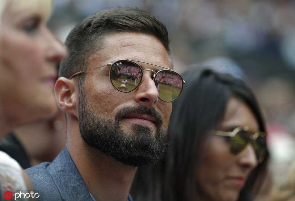 法国神锋吉鲁置身温网中央球场看台，神情专注凝视场内，络腮胡在阳光下显得格外有型，仿佛在研判一场没有越位线的顶级对决。