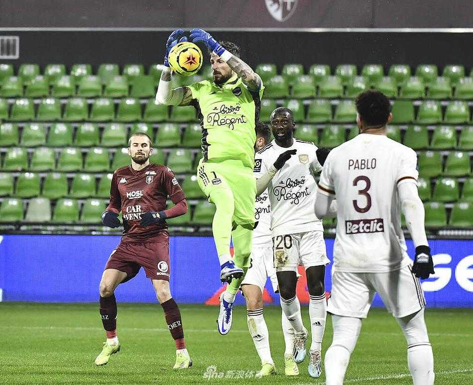 圣塞弗伦球场看台上，一位身穿梅斯主场球衣的球迷在雨中挥舞着围巾，他的脸上写满了期待与焦虑，身后的球迷看台则是人潮涌动，气氛热烈。