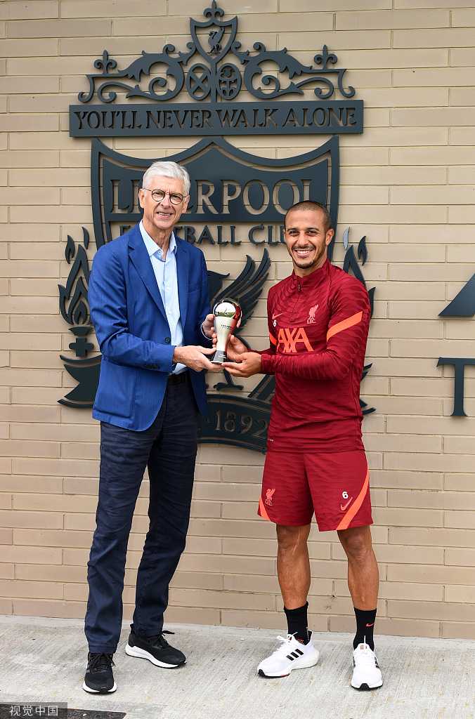 克洛普从温格手中接过FIFA最佳教练奖杯，两人手捧奖座并肩合影，身后是利物浦的训练器材，这一刻胜负已分，唯有敬意长存。