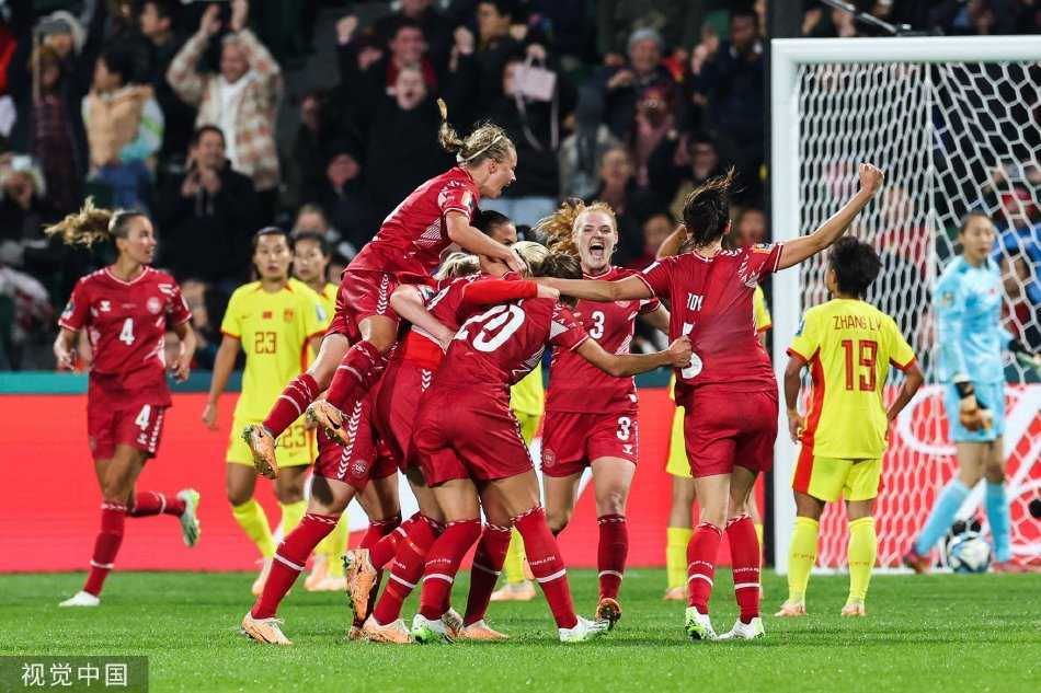 终场哨响瞬间，中国女足姑娘们神情落寞地望向记分牌，疲惫与不甘写满脸庞，背景中庆祝的丹麦队形成了鲜明对比。