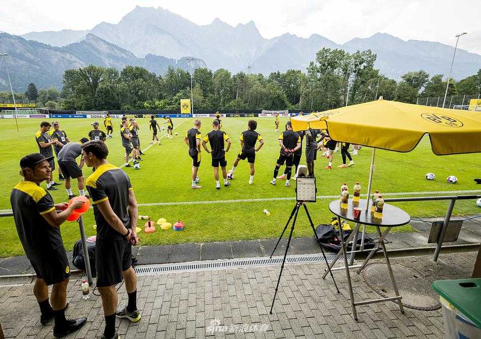 哈兰德在训练中露出标志性的笑容，阳光洒在他的脸上，背景是湛蓝的天空和白云，这位挪威前锋正享受着瑞士的夏日阳光