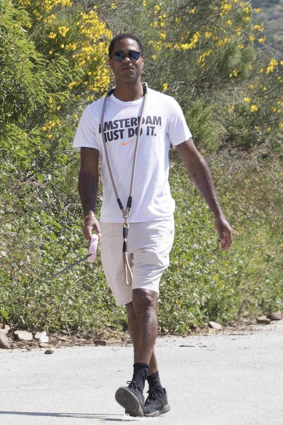 阳光洒在小克鲁伊维特略带微笑的侧脸上，他一只手插在裤兜里，另一只手轻松地握着狗绳，展现出球场之外的帅气与亲和力