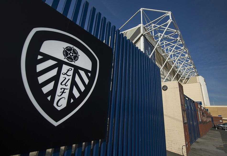 在球员通道入口处，巨大的利兹联队徽悬挂于墙上，通道深处透出光亮，仿佛连接着现实与荣耀的时空隧道。旁边的广告牌上清晰地印着