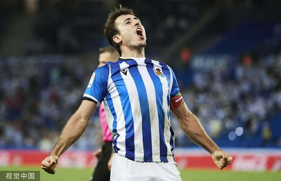 年轻的皇家社会球员在拼抢中毫不畏惧，他的眼神中充满了对胜利的渴望和对赛场的专注。