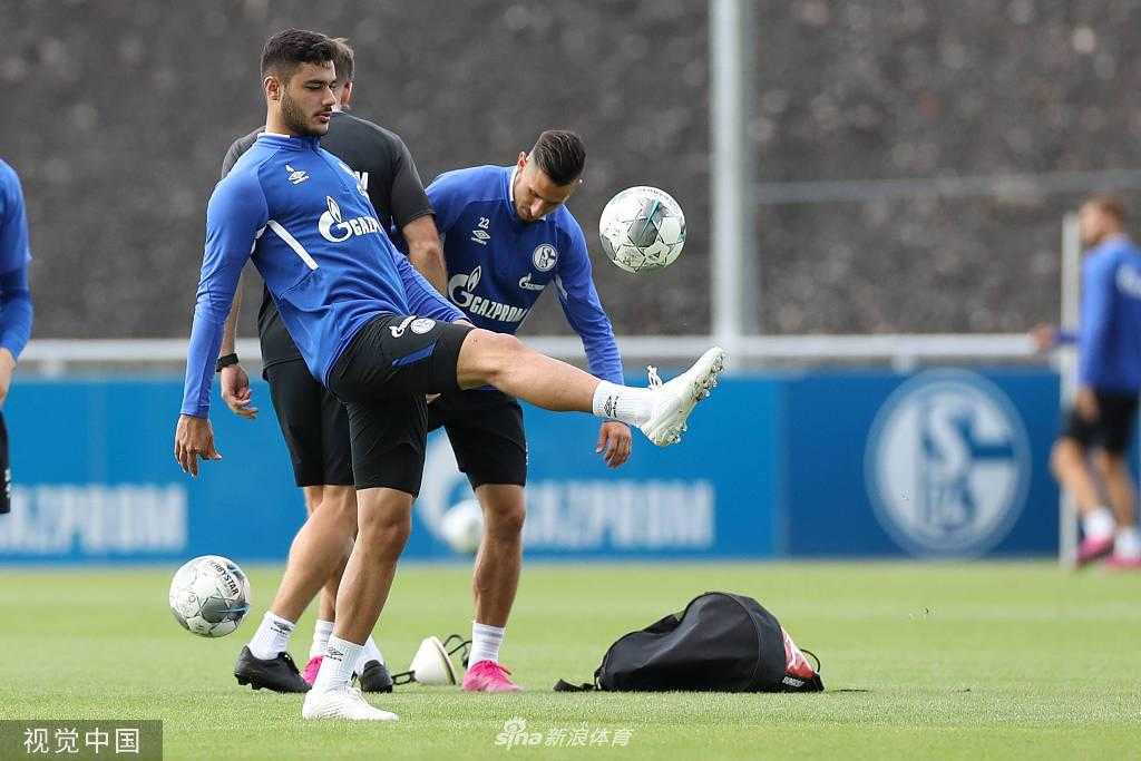 训练间歇，两位沙尔克球员肩并肩走在草坪上，他们神情专注地交流着刚才的配合心得，身后的看台诉说着这座球场的辉煌历史。