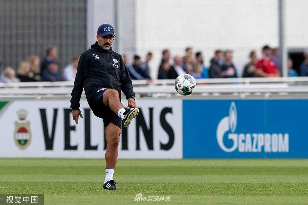 烈日下，一名沙尔克球员正进行冲刺跑训练，他咬紧牙关，手臂有力地摆动，肌肉线条在阳光下清晰可见，全力冲向象征终点的标志物。