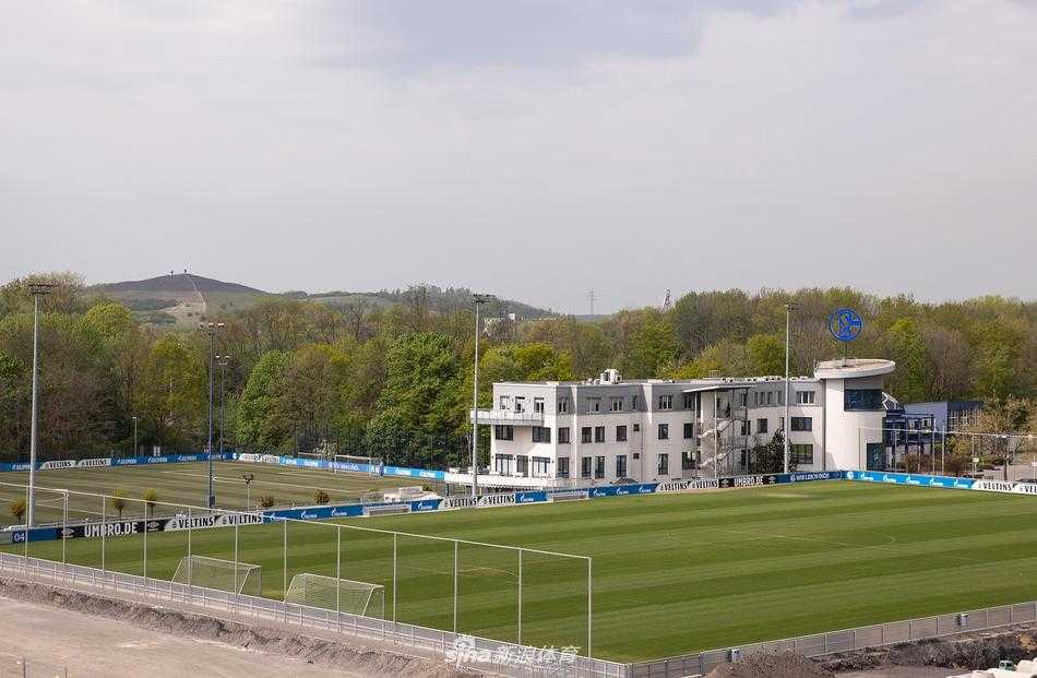 从另一个角度看总部，一列现代化的有轨电车静静驶过站点，车身上醒目的沙尔克04蓝色队徽与远处俱乐部的办公楼遥相呼应，仿佛将这座矿业城市的足球血脉，通过铁轨延伸至每一个角落。