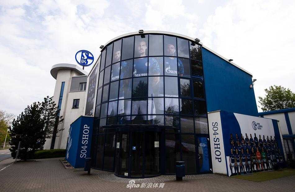 春日午后，沙尔克04总部办公楼在蓝白相间的围栏后显得静谧而庄严，建筑立面上巨大的俱乐部标识，默默守望着空荡荡的街道，仿佛在诉说着那段没有球迷欢呼的寂静时光。