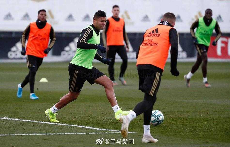 皇马医疗团队的一名成员正细心地整理着训练器材，远处的体能教练正带领着少数几名非伤病球员进行核心力量训练，气氛严肃而专注。