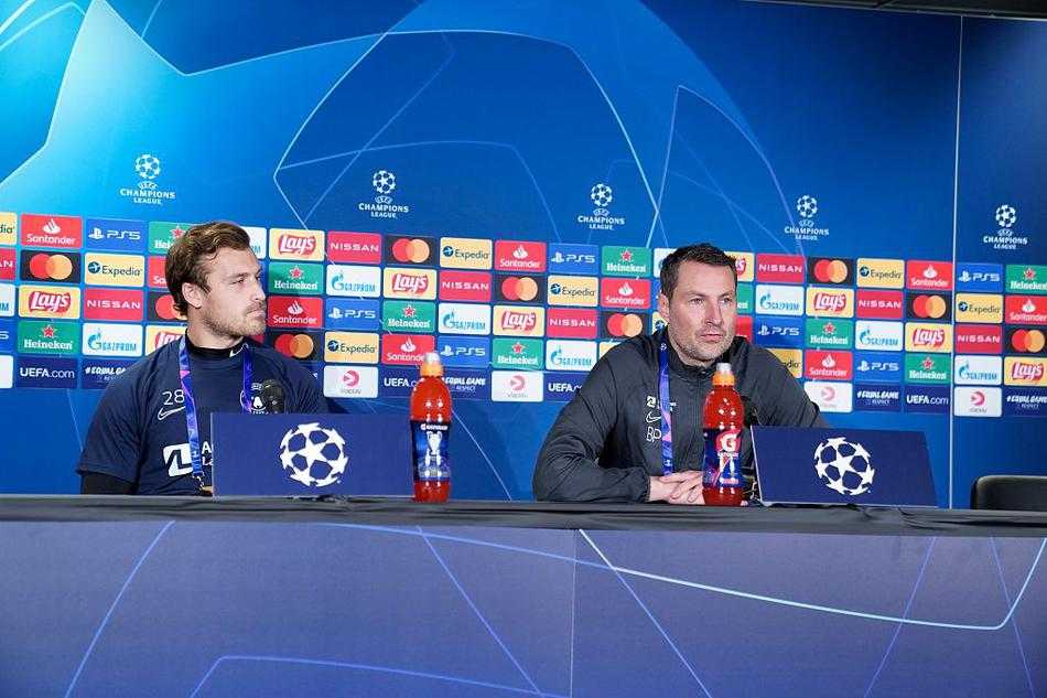 主教练神情专注，在话筒前阐述着比赛哲学，身后的队徽在灯光下格外醒目，仿佛在诉说着丹麦足球的坚韧与智慧。