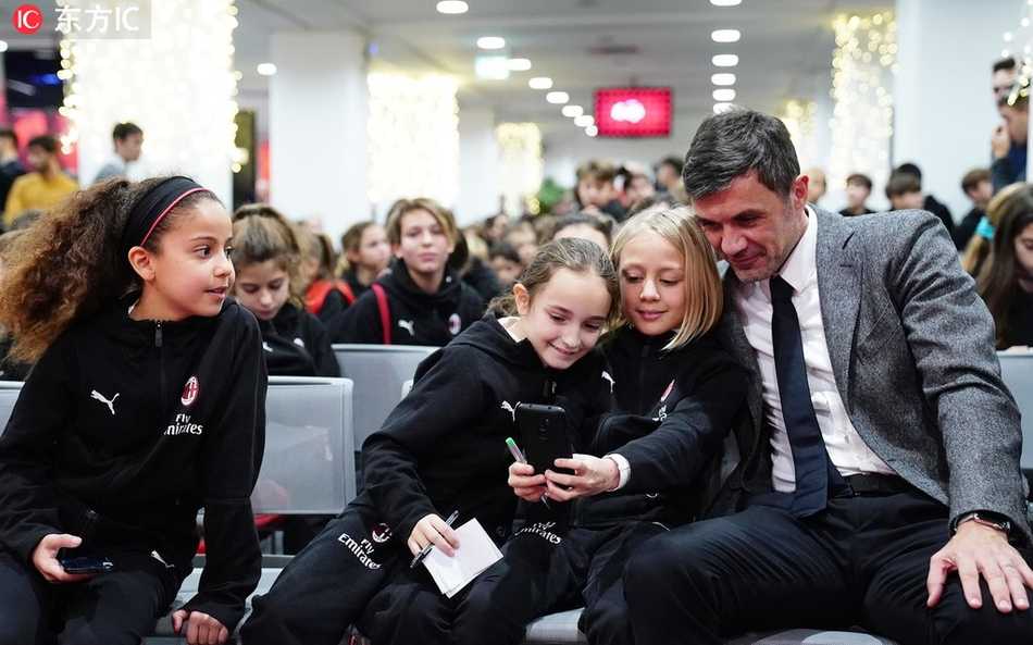 红黑军团的未来希望:AC米兰青年队的圣诞传承 一名年纪最小的小球员坐在圣诞老人(由助理教练装扮)的腿上,略显羞涩地讲述着自己的足球梦想,周围围坐的队友们纷纷鼓掌,眼中满是鼓励与期待。