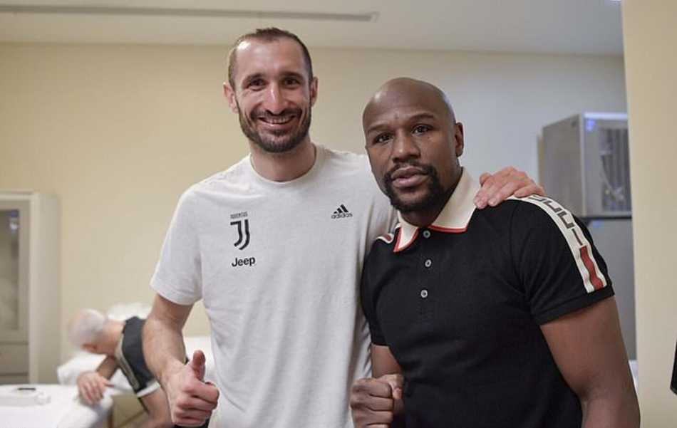 C罗与梅威瑟在更衣室通道相逢，两人紧紧握手致意，C罗露出标志性的迷人微笑，梅威瑟则微微颔首，两位不同时代的体坛霸主周围闪光灯亮成一片，定格了历史性的一刻。