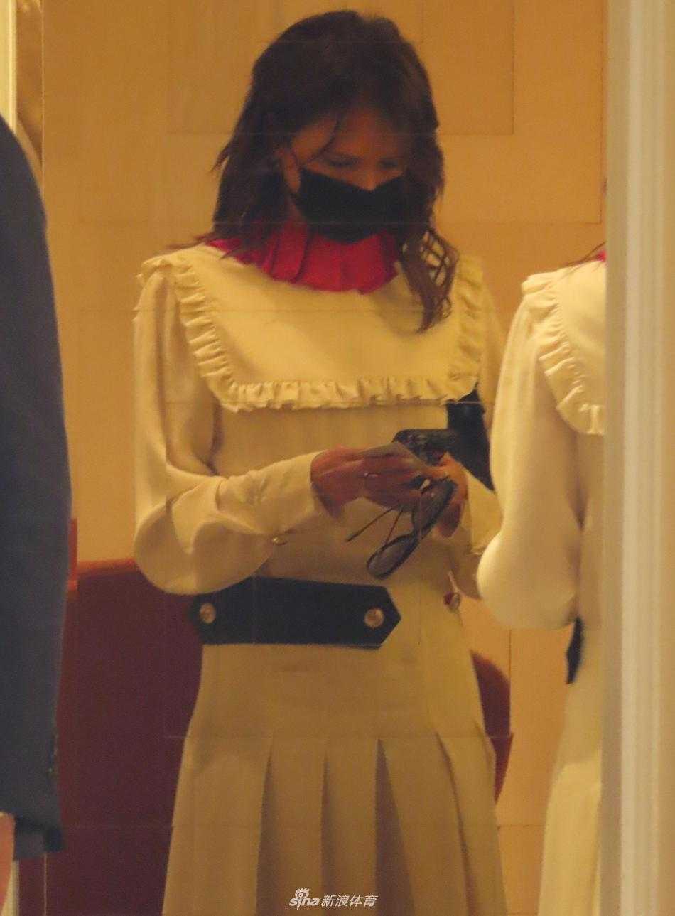 另一角度下的维多利亚，白色长裙的裙摆在行走中随风飘动，展现出优美的流动感，她手持手机，似乎正在处理繁忙的工作，完美诠释了现代职业女性的利落形象。