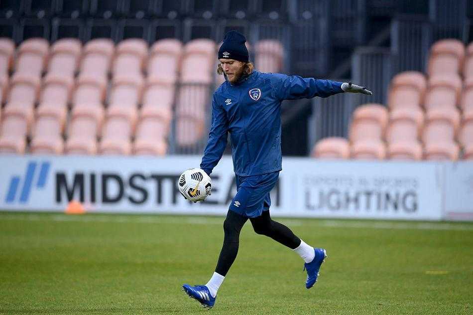 在清晨的薄雾中，爱尔兰球员们正在进行高强度分组对抗，一名中场球员刚完成一次干净利落的铲抢，起身后立即挥手指挥队友站位，眼神中透露出与训练服上徽章相匹配的坚定。