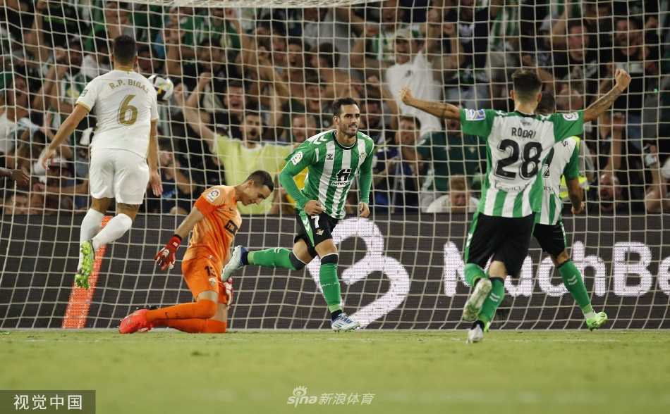 贝蒂斯主帅佩莱格里尼在场边凝神观赛，手托下巴陷入思考，身后的替补席和绿茵场形成生动的背景