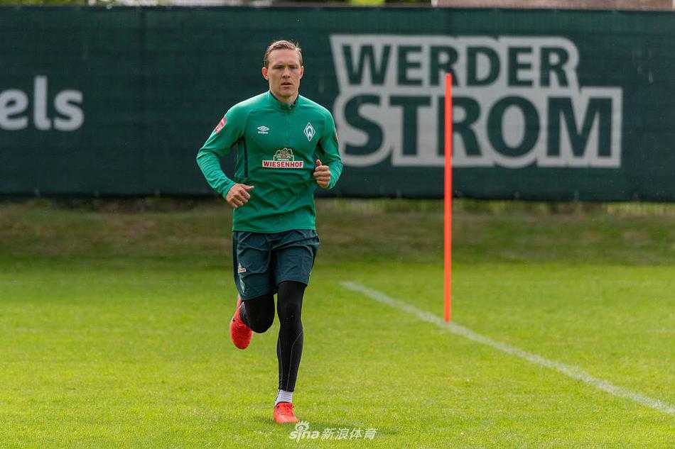 球员独自进行带球绕杆训练，阳光洒在绿色的草皮上，背影显得坚毅而决绝