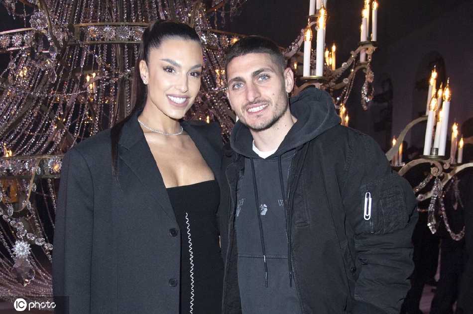 维拉蒂与妻子在人群中缓步前行，他体贴地调整步伐以适应穿着高跟鞋的妻子，杰西卡则挽着他的手臂，两人一边走一边轻松交谈，周围繁华的时尚景象成为了他们恩爱背影的最佳衬托。