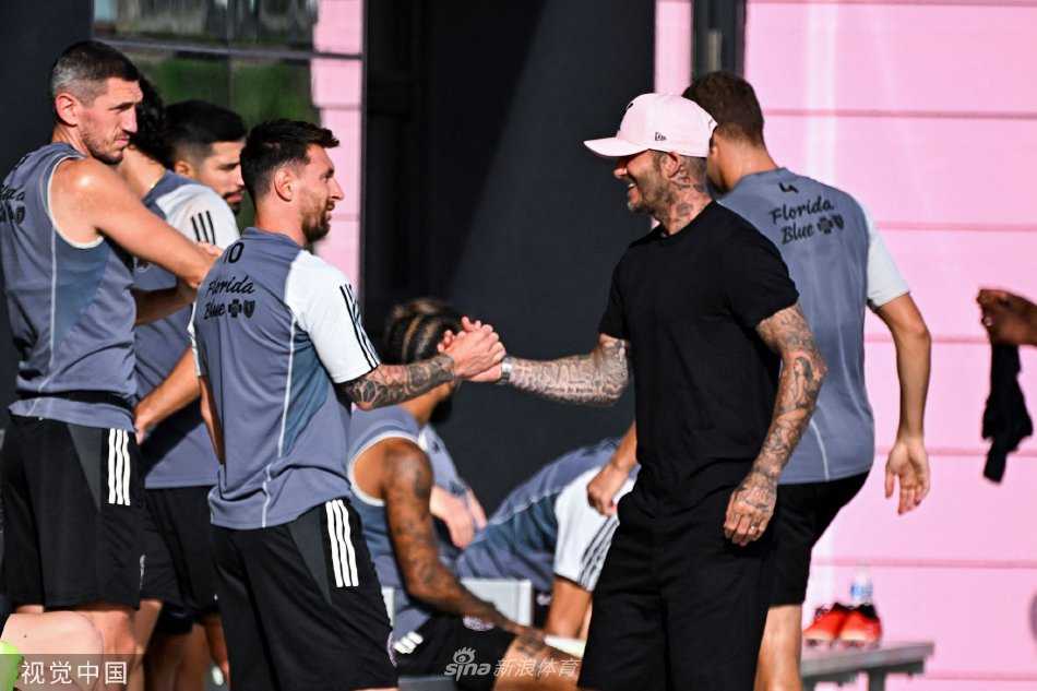 大卫·贝克汉姆一身休闲装扮，面带标志性笑容，与身旁的莱昂内尔·梅西轻松交谈，两人在训练场边形成一道独特的风景。