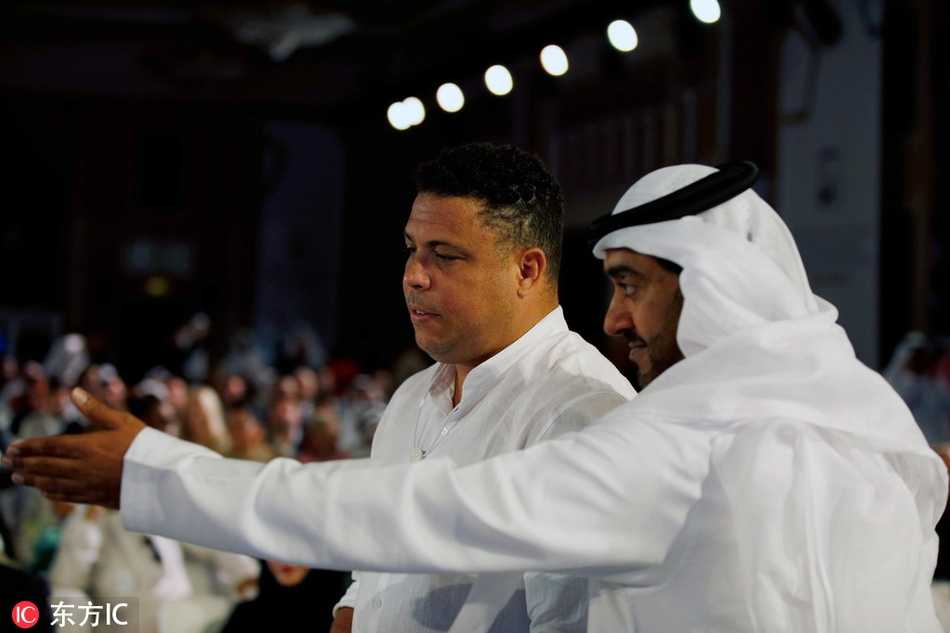 在迪拜体育大会的走廊上，罗纳尔多身着一袭深色正装，笑容满面地侧身与身旁的加图索交谈，两人的眼神中透露出老友重逢的喜悦与专注。