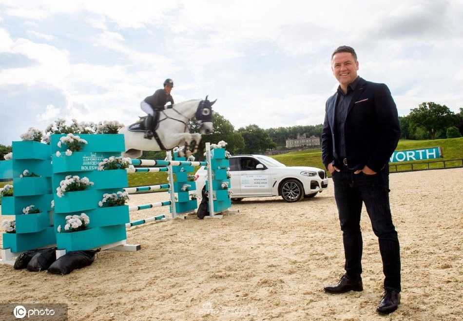 阳光和煦的午后，迈克尔·欧文身着休闲西装，微笑着与赞助商代表在波尔斯沃斯庄园的绿色草坪上亲切交谈，远处城堡的塔楼为背景增添了一份古典韵味。